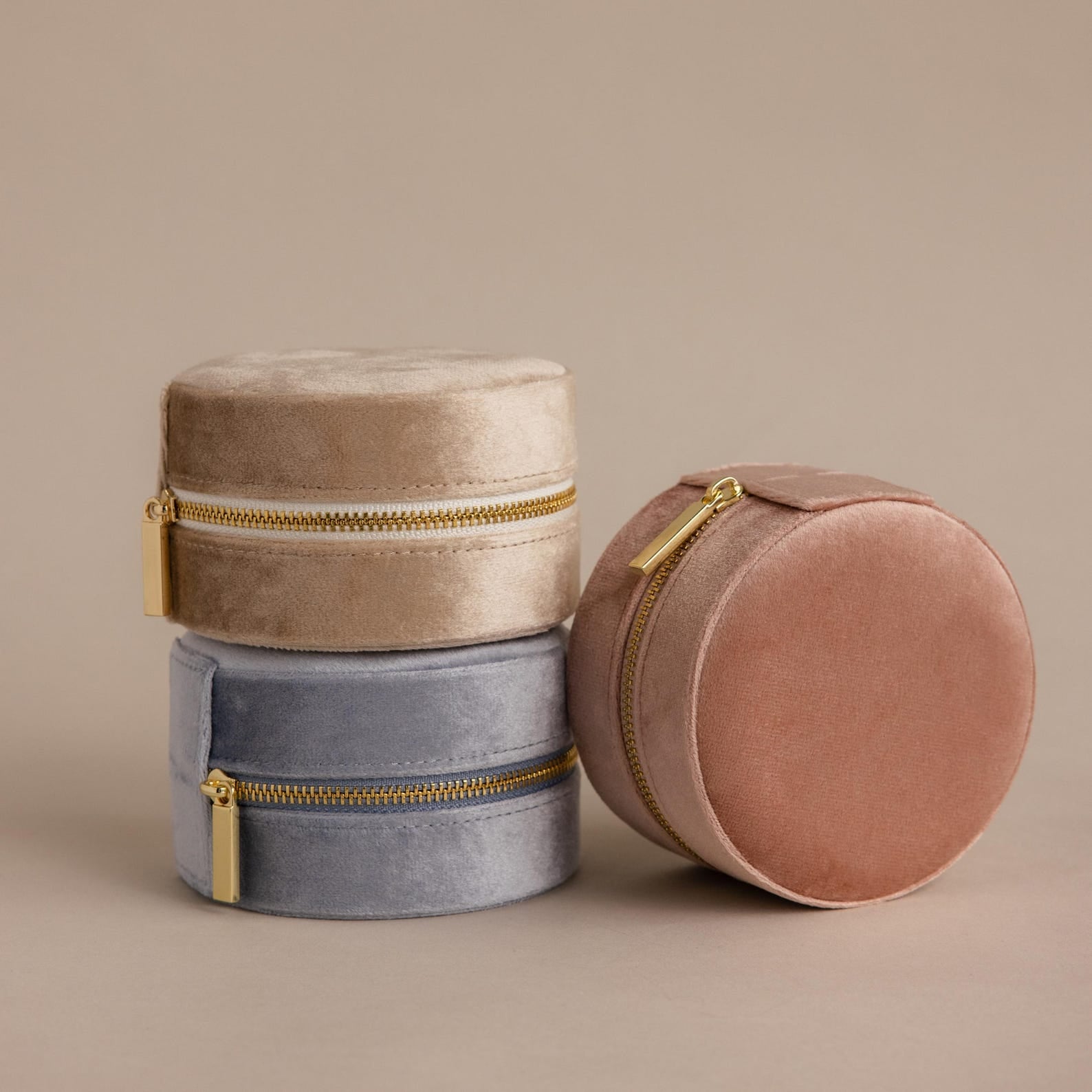 Three Round Velvet Jewelry Cases—perfect as minimalist jewelry boxes or travel organizers—come in beige, blue, and pink. These elegant Round Velvet Jewelry Cases are attractively stacked on a neutral background.