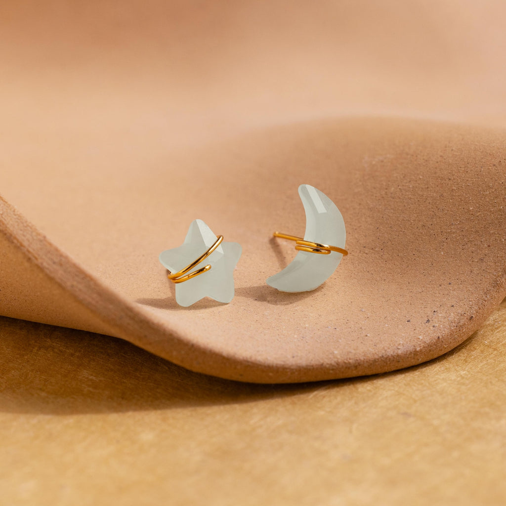 Aquamarine Moon & Star Studs shaped like a star and crescent moon rest on a textured beige surface—perfect dainty stud earrings for adding everyday sparkle.