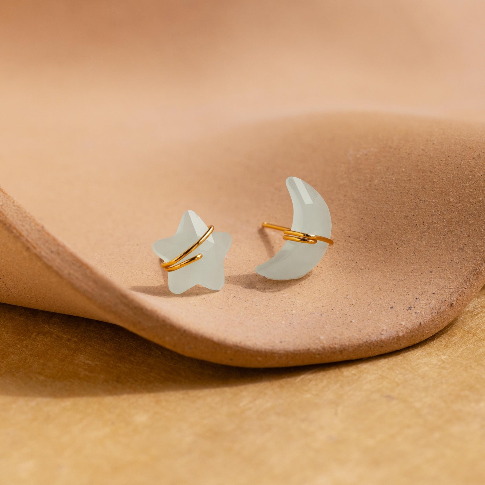 Aquamarine Moon & Star Studs shaped like a star and crescent moon rest on a textured beige surface—perfect dainty stud earrings for adding everyday sparkle.