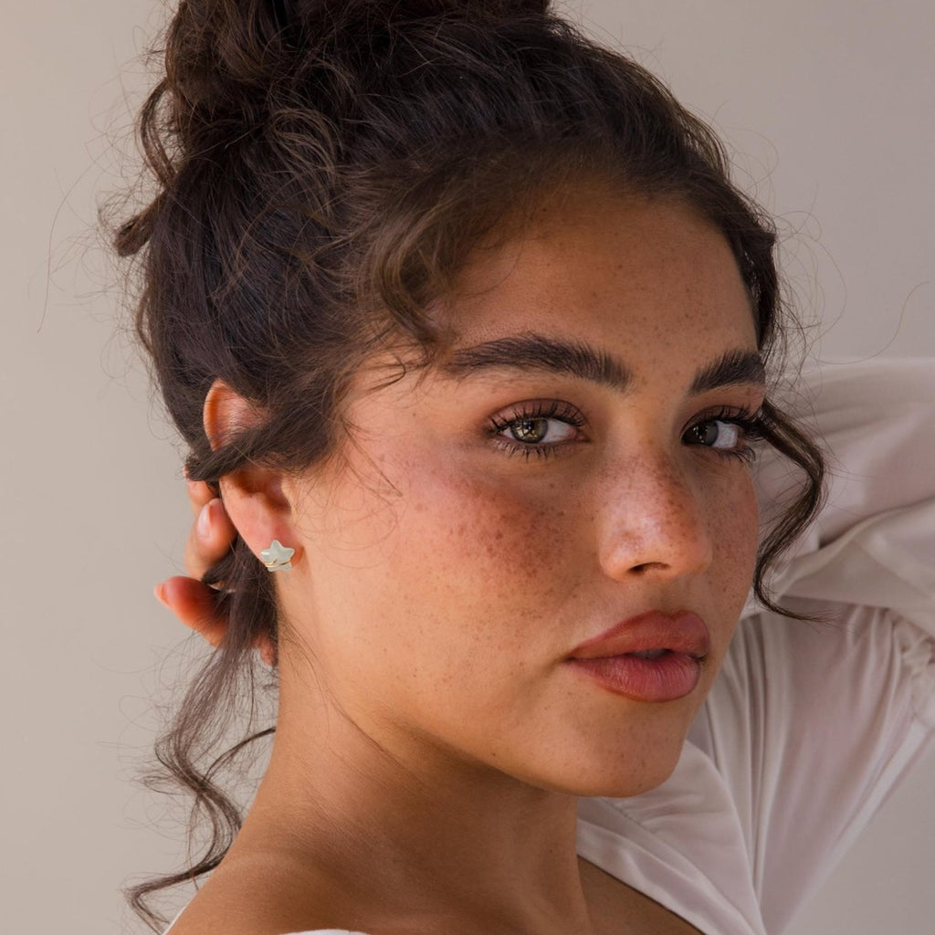 Woman with curly hair in a bun, wearing a white top and Aquamarine Moon & Star Studs, gazes at the camera.