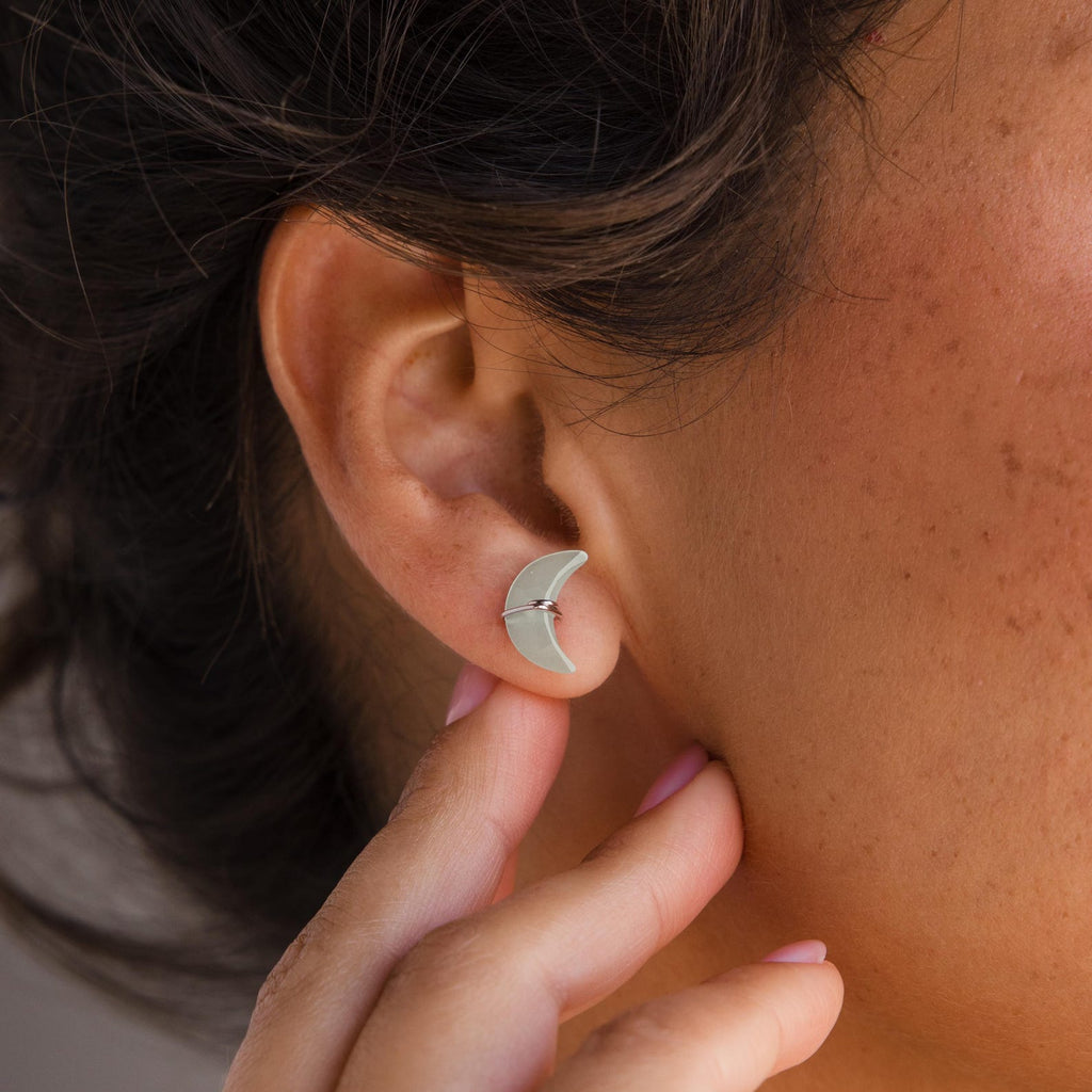 A person touching their ear adorned with Aquamarine Moon & Star Studs.