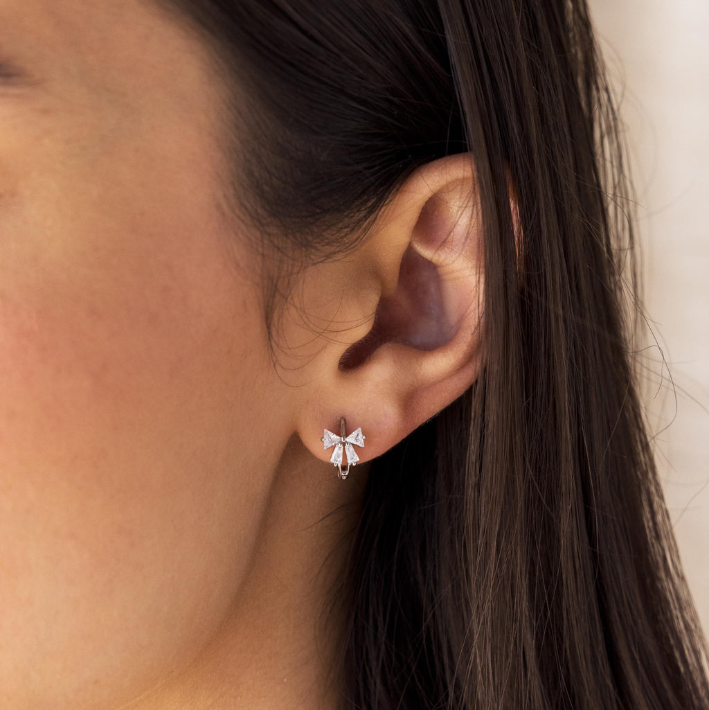 Close-up of model wearing Diamond Ribbon Bow Charm Huggie Earrings in Sterling Silver.