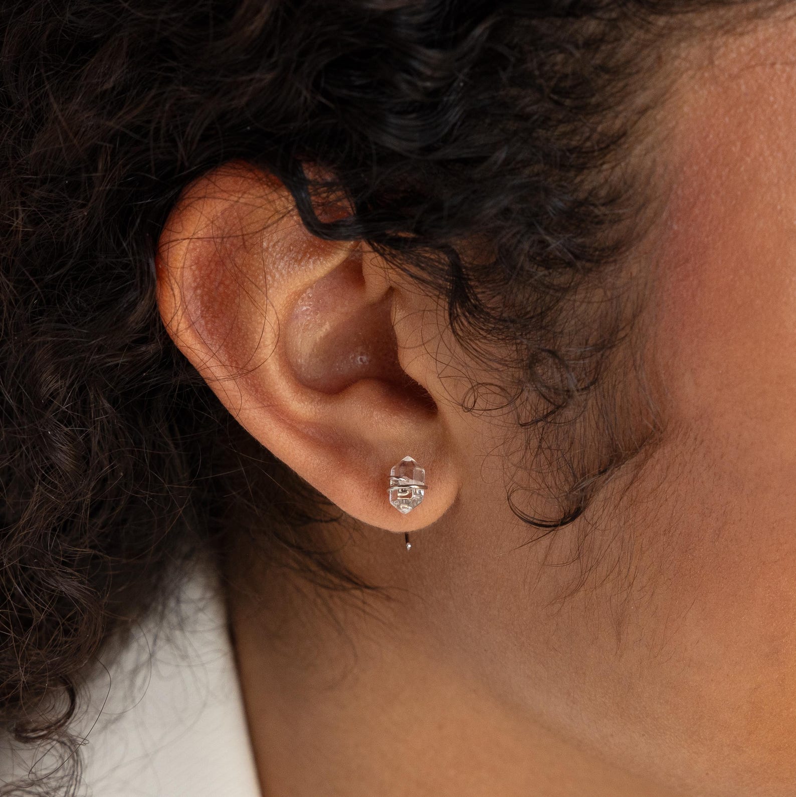 Close-up of a person’s ear wearing the Herkimer Diamond Threaders, delicate and bohemian earrings featuring a small silver design.