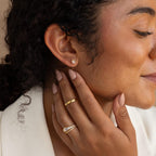 A woman smiles, touching her ear with a manicured hand while wearing gold rings and nature-inspired studs paired with delicate Herkimer Diamond Threaders.