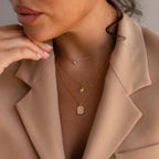 Woman wearing a beige blazer and layered gold necklaces, including a Pavé Gemstone Initial Necklace featuring the letter K.