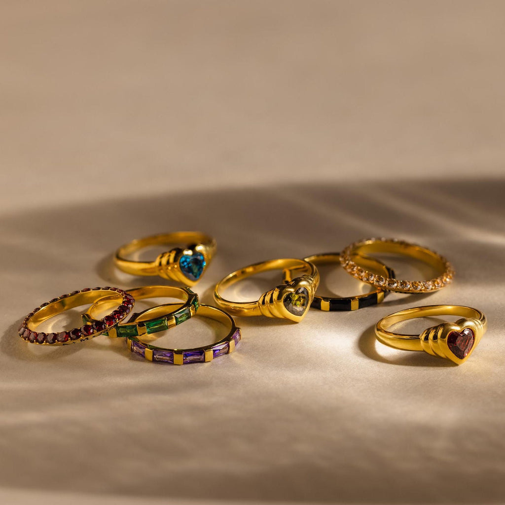 Eight Half Eternity Birthstone Rings are arranged on a beige surface with soft shadows—an elegant choice for an anniversary keepsake.