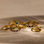 Eight Half Eternity Birthstone Rings are arranged on a beige surface with soft shadows—an elegant choice for an anniversary keepsake.