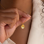 A person holds a Baby Handprint Coin Necklace—a gold pendant engraved with tiny handprints—making it a perfect personalized keepsake and thoughtful gift for new moms.