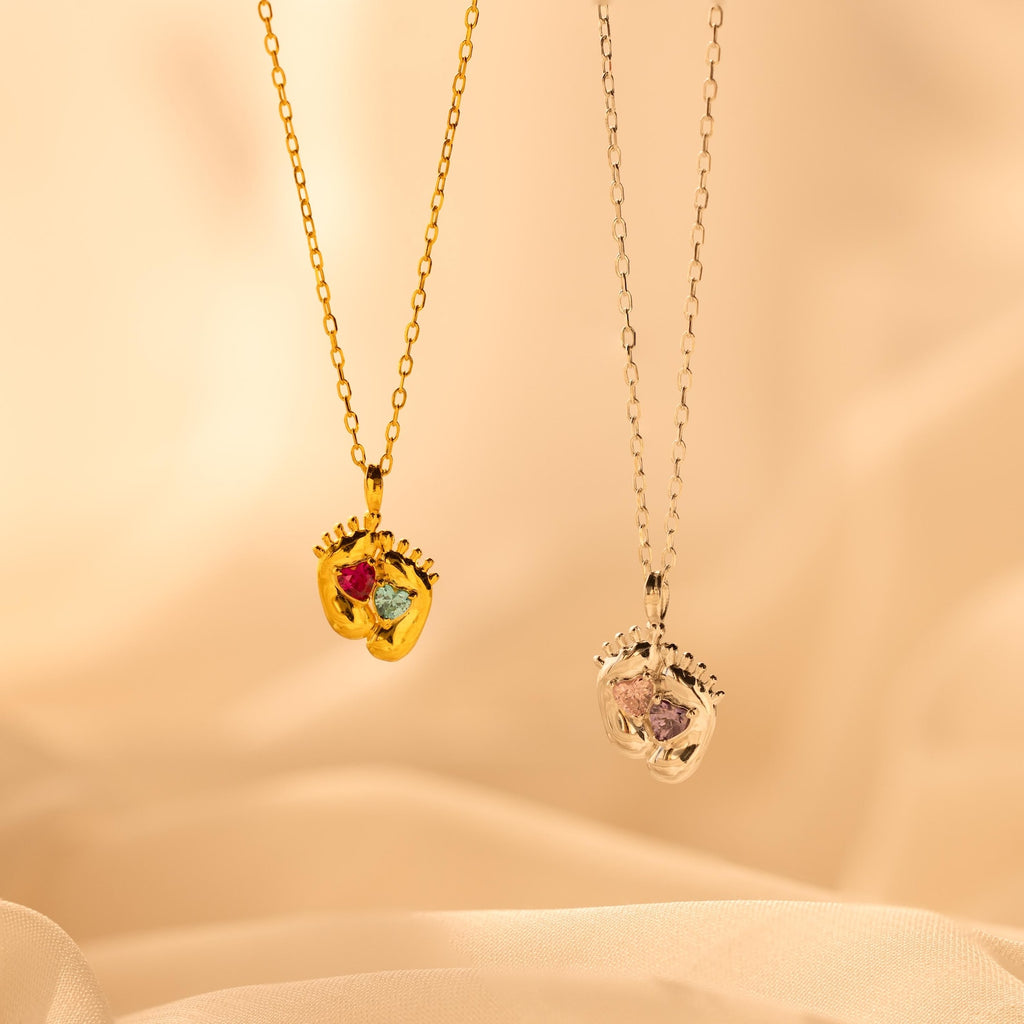 Two Footprint Birthstone Necklaces—one gold with colorful stones, one silver with clear stones—make a perfect parent and child jewelry set or can be worn as a personalized charm necklace.