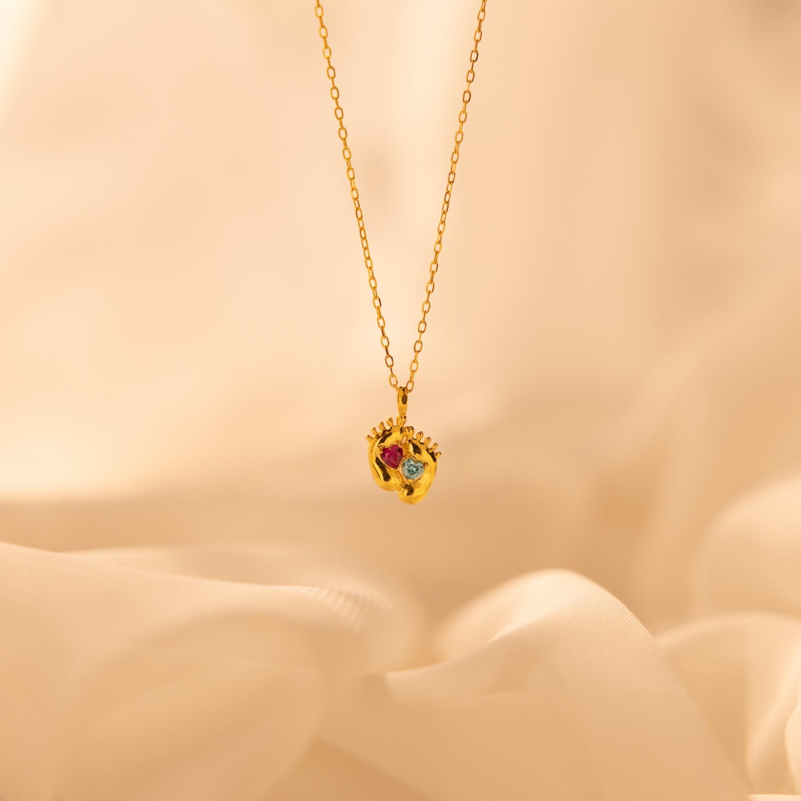 Footprint Birthstone Necklace with a pendant of two baby feet, each set with a birthstone—perfect parent and child jewelry—displayed on a soft beige background.