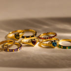 The Birthstone Heart Signet Ring, featuring a heart-shaped gemstone and colorful enamel accents, is beautifully displayed on a neutral surface in warm lighting.