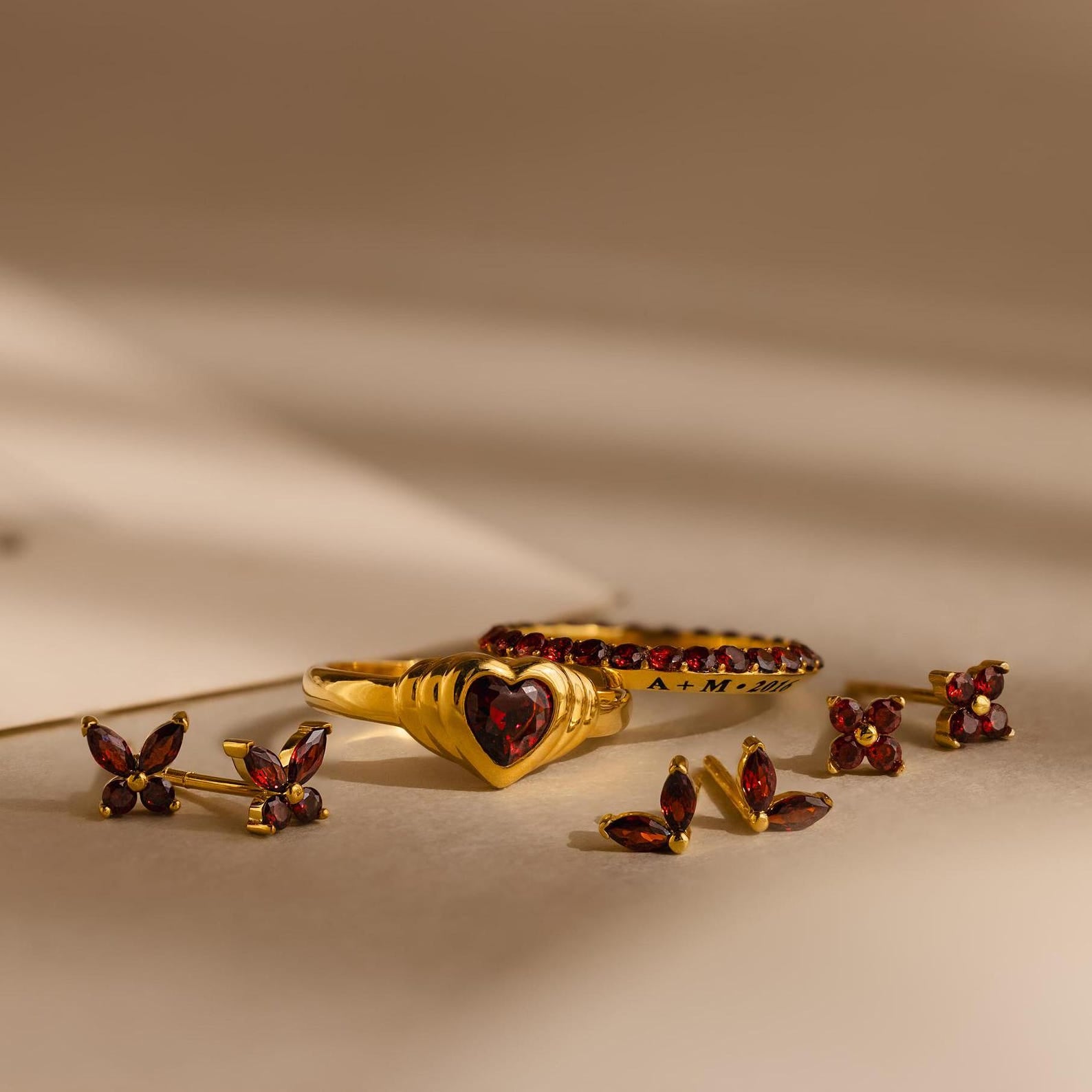 Ivy Flower Birthstone Studs with vibrant red gemstones are displayed on a neutral background with soft shadows.