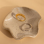 A Ring Size Adjuster rests on a speckled, wavy-edged ceramic dish against a beige background.