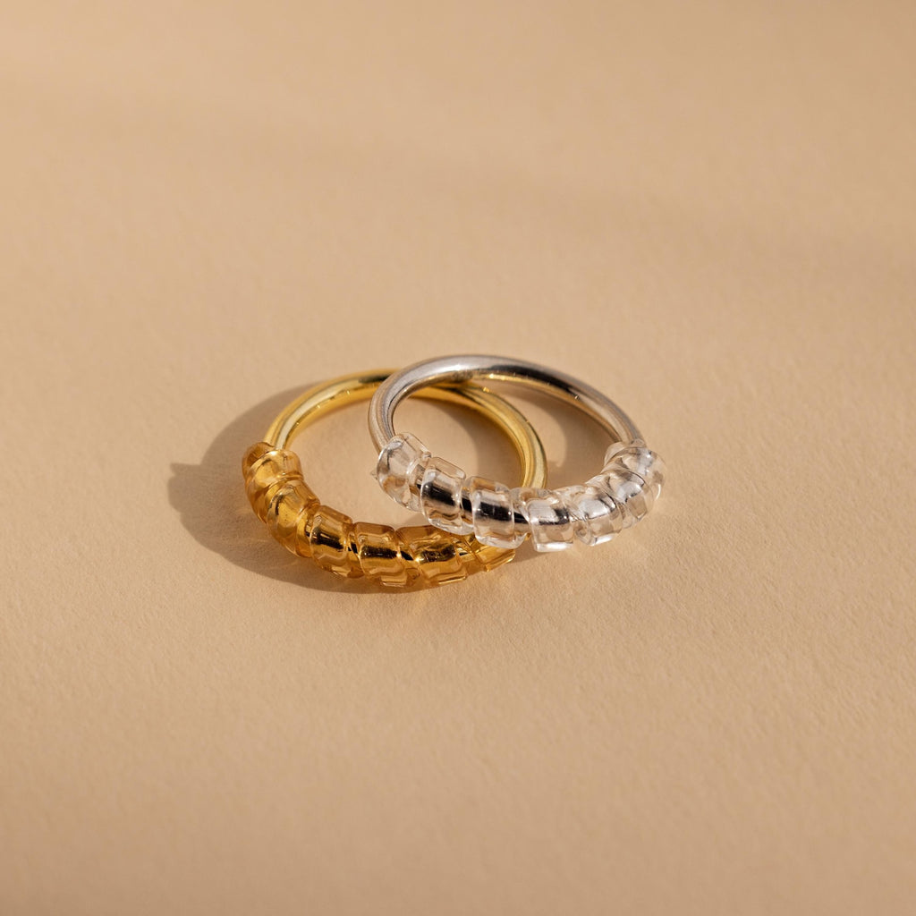Two Ring Size Adjusters, one gold and one silver, are displayed side by side on a smooth beige surface.