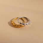 Two Ring Size Adjusters, one gold and one silver, are displayed side by side on a smooth beige surface.