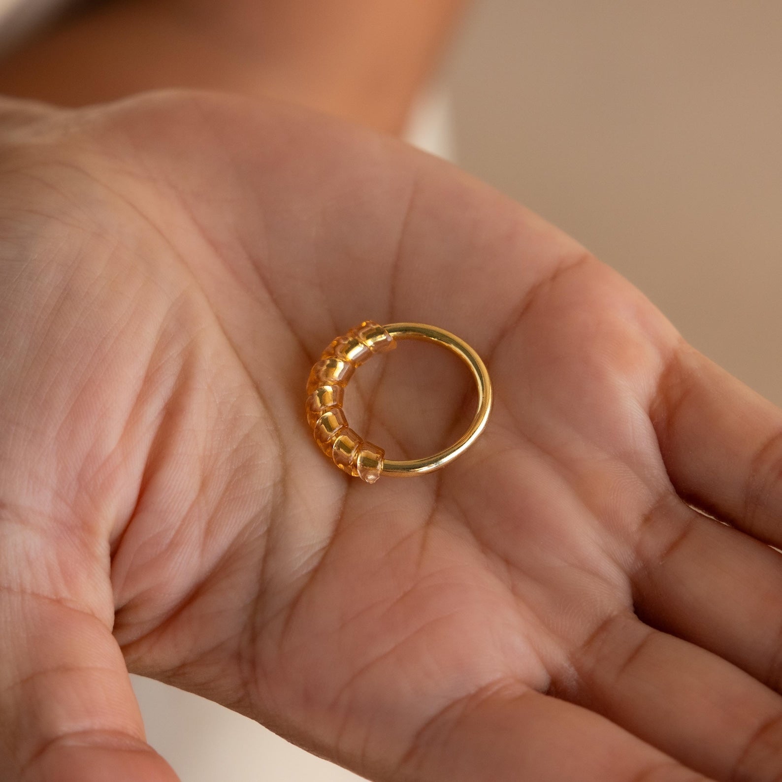 A hand holds the Ring Size Adjuster, a gold ring accessory with a textured, decorative side—ideal for anyone with loose rings or looking for a subtle way to achieve the perfect fit.