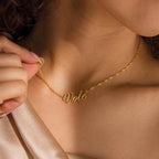A person wears an Essential Vote Necklace featuring a "vote" pendant, holding the chain near their collarbone—a unique gift for voters.