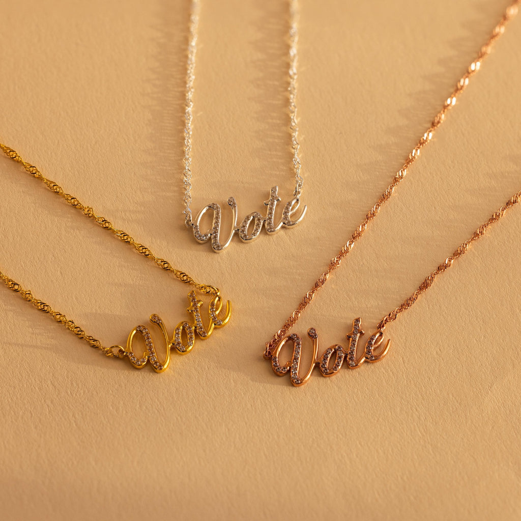 Three Essential Vote Necklaces in gold, silver, and rose gold rest on a beige surface—a meaningful and inspiring gift for voters or anyone who loves a symbolic voting necklace.