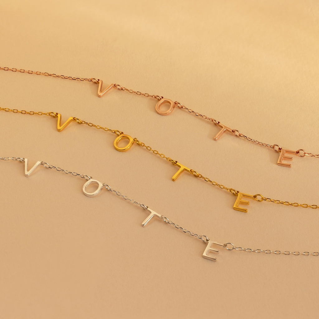 Three delicate Essential Vote Necklaces spell VOTE in gold, rose gold, and silver on a neutral background—a stylish gift for voters.