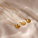 The Baby Handprint Coin Necklace features three gold pendants on delicate chains, displayed on soft, light-colored fabric—an elegant personalized keepsake and a perfect gift for new moms.