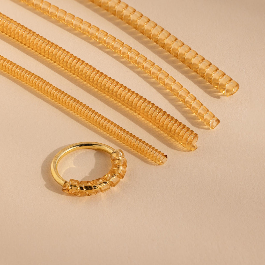 The Ring Size Adjuster includes four coiled, translucent tubes displayed on a beige surface with soft lighting—perfect for anyone needing to tighten loose rings.