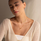 Woman with closed eyes, wearing an Elegant Birthstone Name Necklace and a cream knit top, sits in soft natural light.
