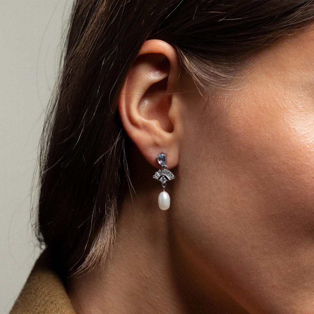 Close-up of a woman's ear wearing Aquamarine Pearl Drop Earrings—silver earrings with blue aquamarine stones and a dangling white pearl, perfect for adding vintage glamour or as wedding jewelry.