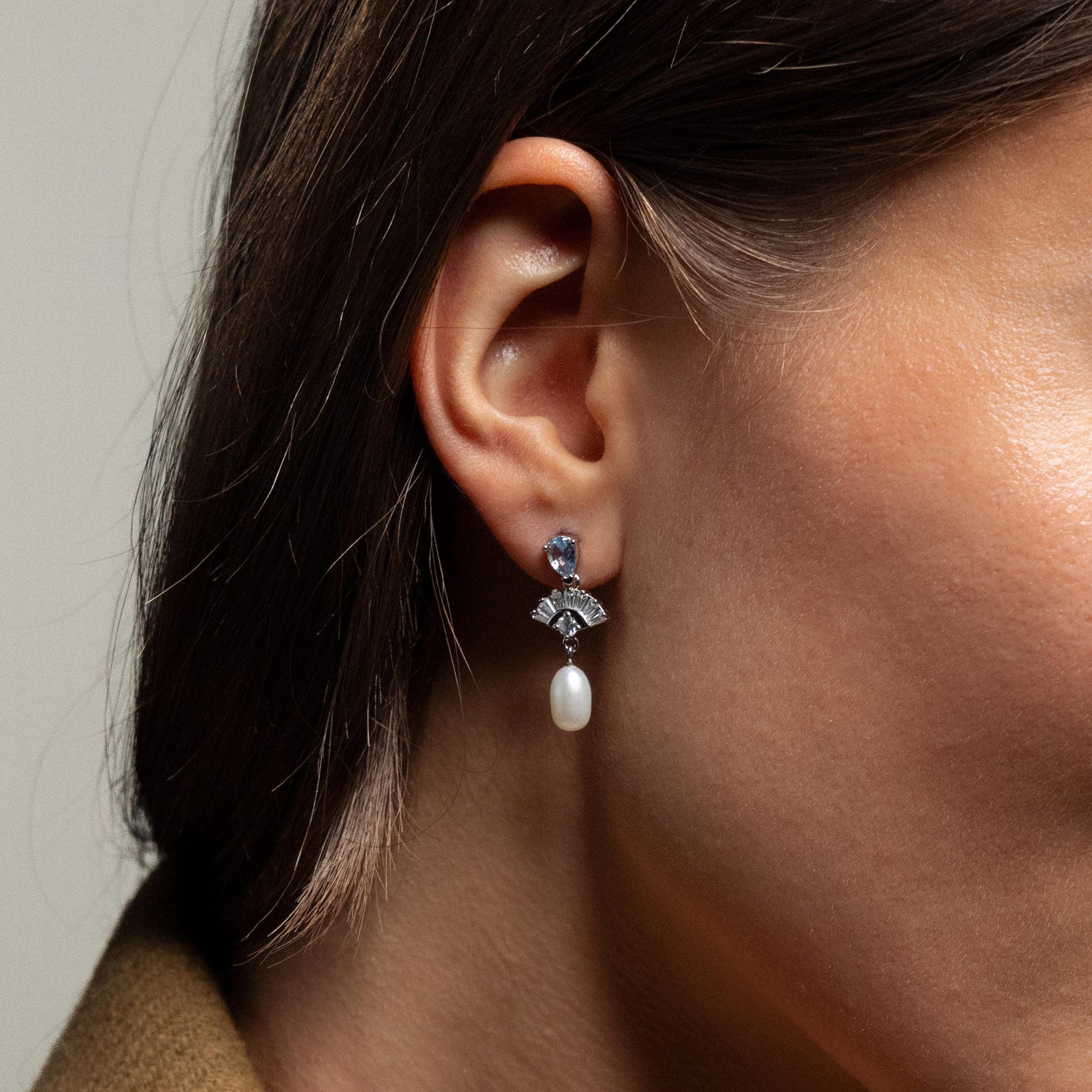 Close-up of a woman's ear wearing Aquamarine Pearl Drop Earrings—silver earrings with blue aquamarine stones and a dangling white pearl, perfect for adding vintage glamour or as wedding jewelry.