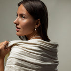 A woman with brown hair looks to the side, wearing Art Deco Pearl Drop Earrings and a cream shawl draped over her shoulders.