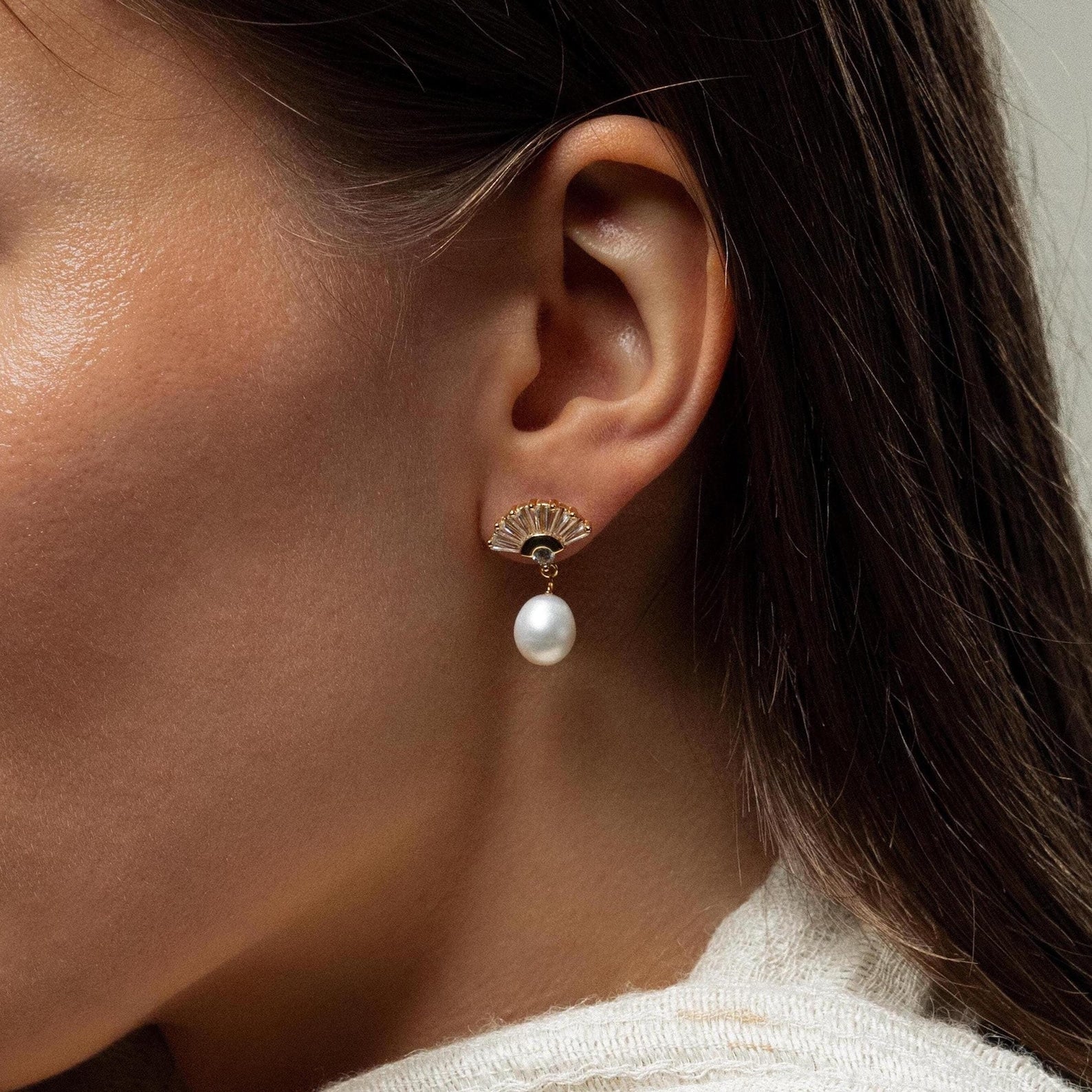 Close-up of a woman's ear wearing Art Deco Pearl Drop Earrings, featuring a gold fan-shaped design with a dangling pearl for vintage glamour.