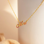 The Elegant Birthstone Name Necklace features a "Mrs" script pendant accented with pink stones, perfect as personalized or custom jewelry, showcased against a soft background.
