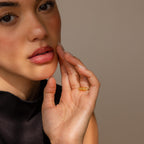 A woman with natural makeup wears a gold ring fitted with the Ring Size Adjuster for loose rings, paired with a sleeveless black top against a neutral background.