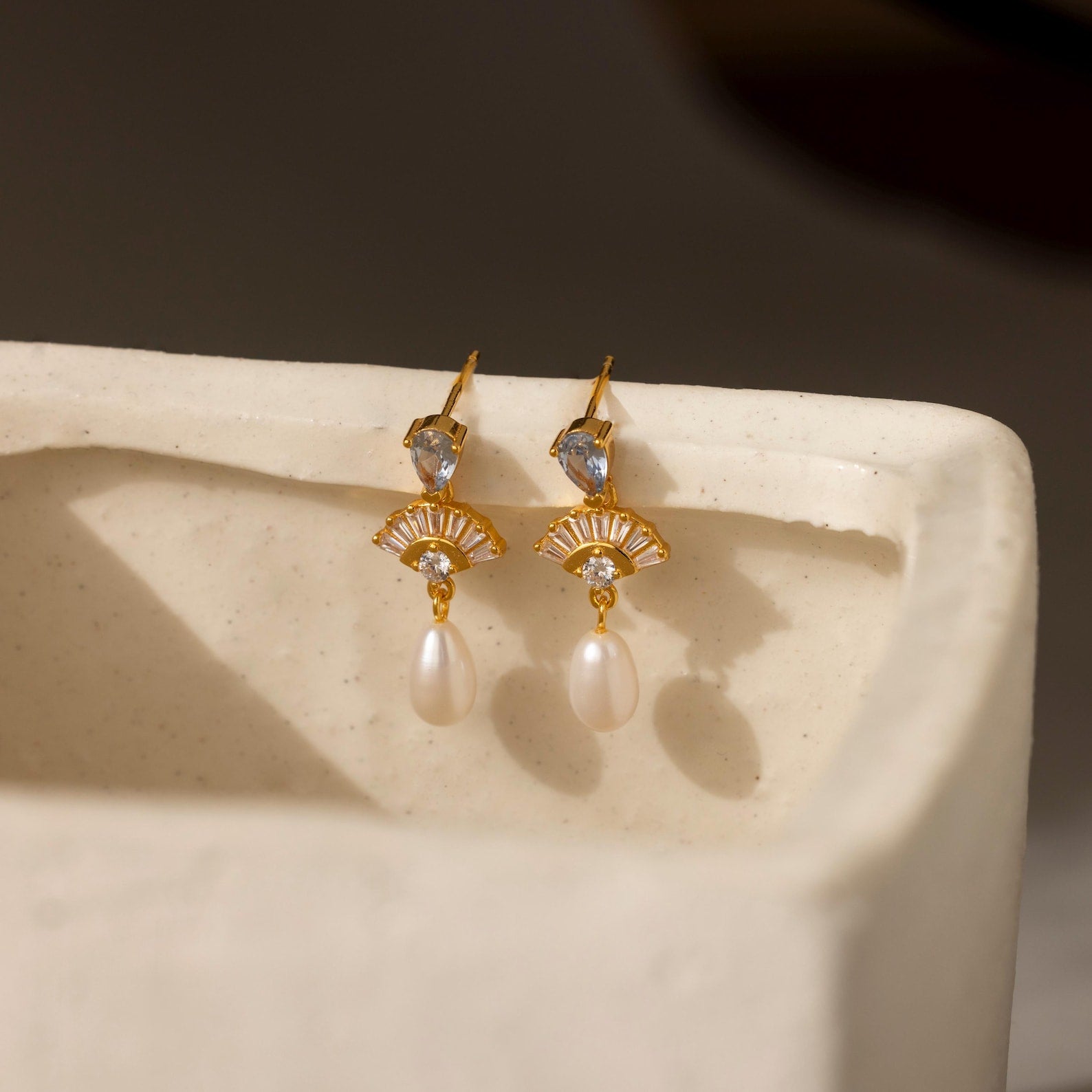 Aquamarine Pearl Drop Earrings evoke vintage glamour with crystal and pearl drops, perfect for weddings, showcased on a cream-colored textured surface.