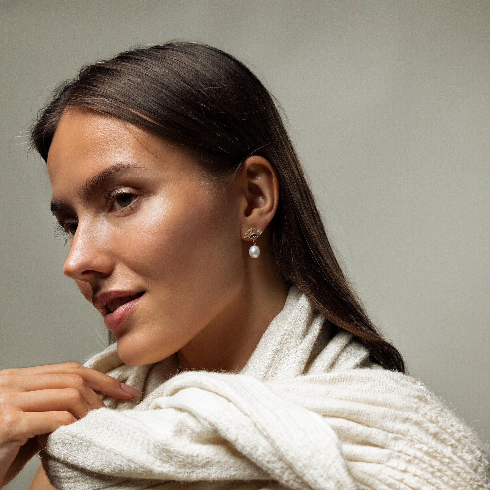 A woman with a white scarf around her neck wears Art Deco Pearl Drop Earrings, adding a touch of timeless style to her look.