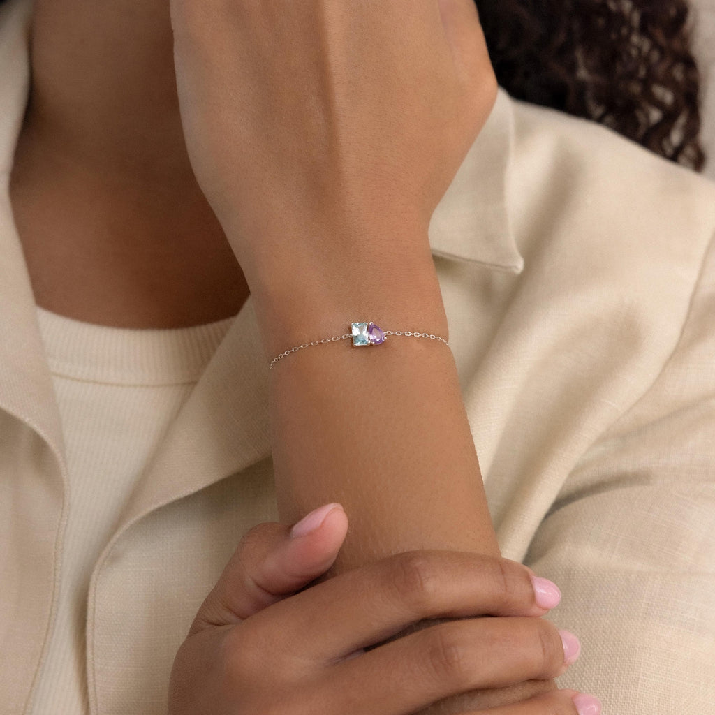 A person wears the Toi et Moi Birthstone Bracelet, which features a slim silver band and a customizable rectangular birthstone gem on their wrist.
