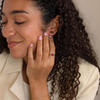 A woman with curly hair smiles, wearing vibrant Toi et Moi Birthstone Earrings and a matching gemstone ring.
