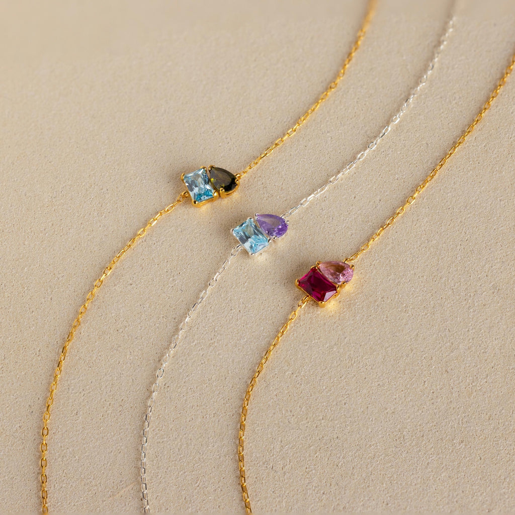 The Toi et Moi Birthstone Bracelet features delicate chains with customizable gemstones and colorful charms, perfect for creating a personalized bracelet look.