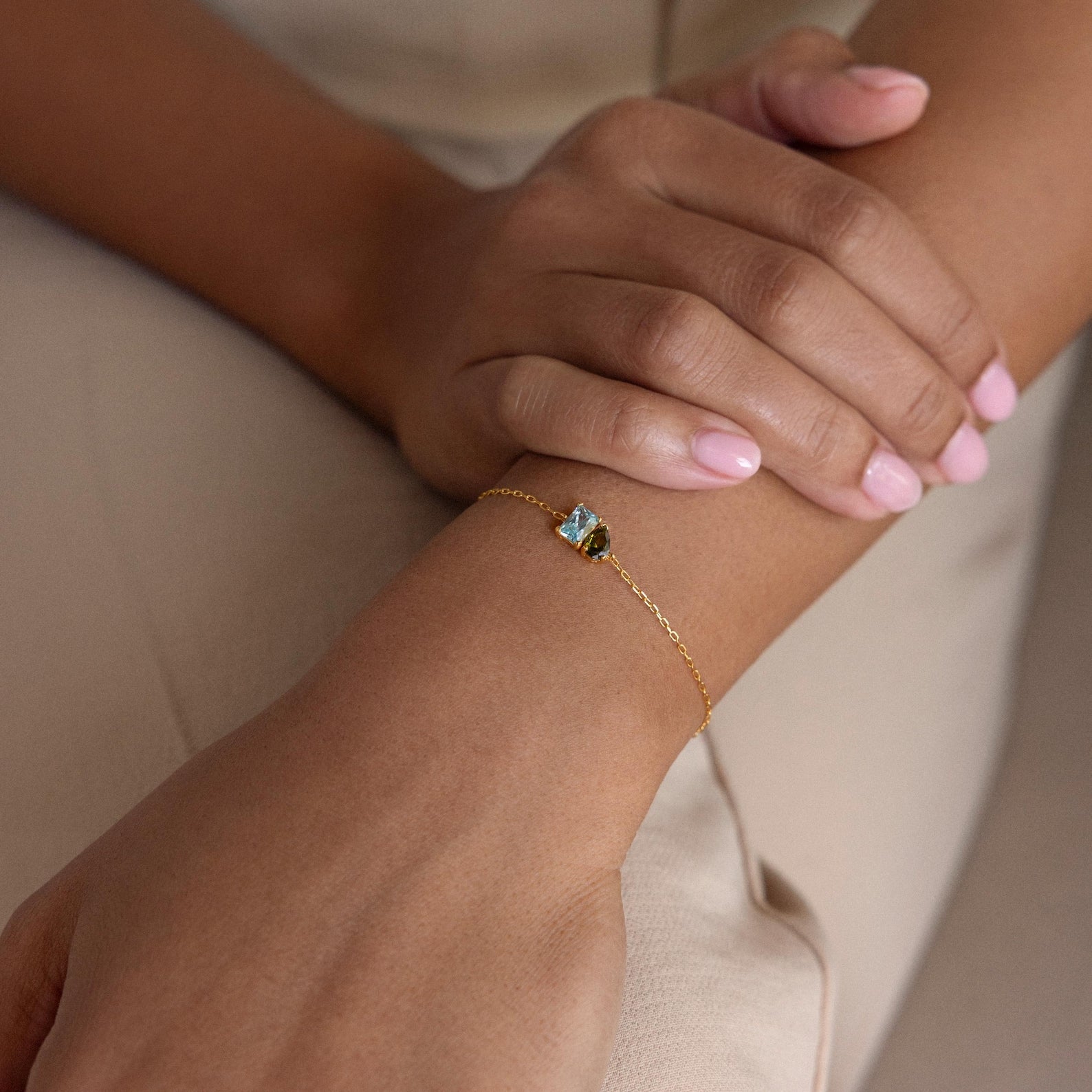 A hand with light pink nails wears the Toi et Moi Birthstone Bracelet, a delicate gold personalized piece featuring a small customizable gemstone on the wrist.