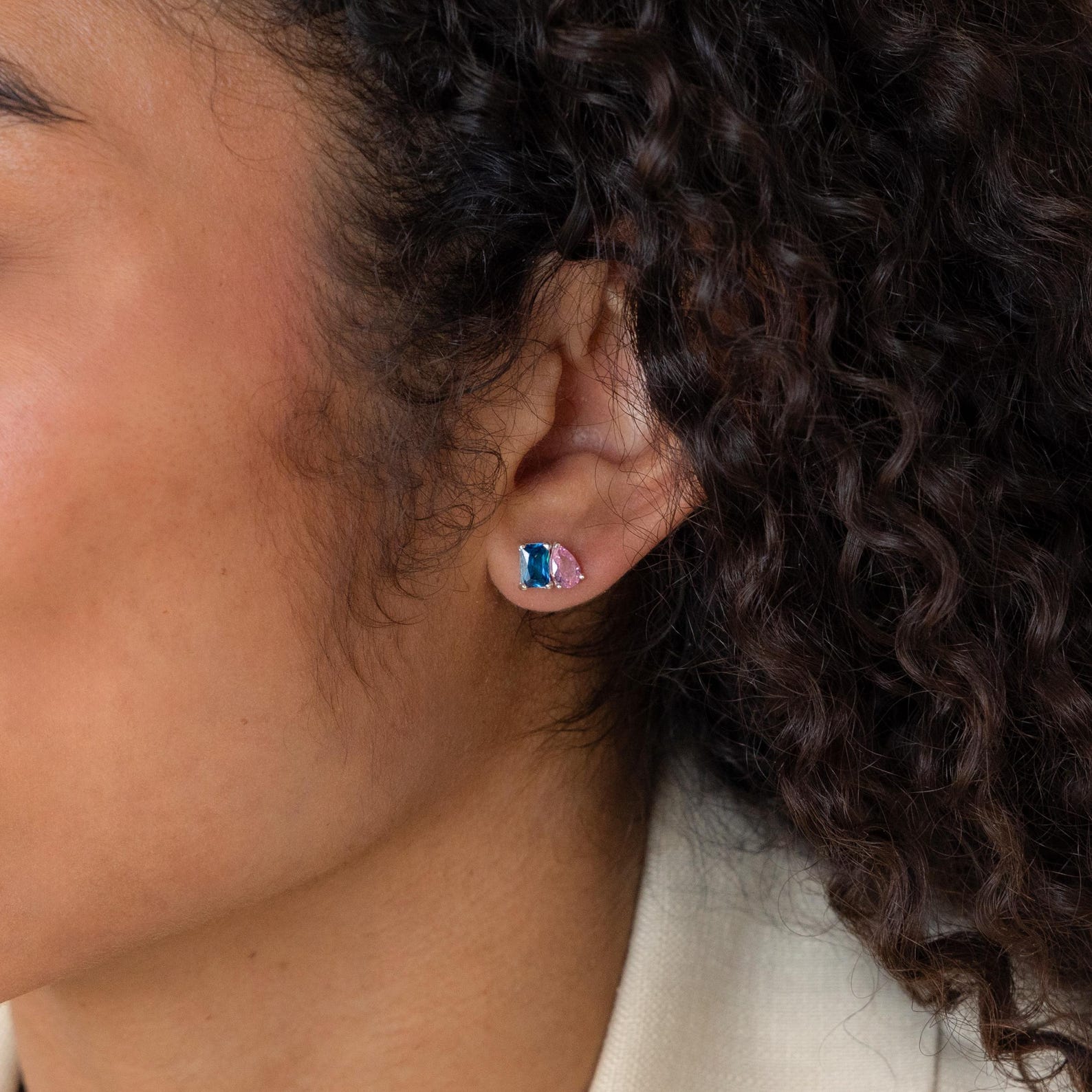 Close-up of a person with curly hair wearing the Toi et Moi Birthstone Earrings, featuring small blue and pink gemstones.