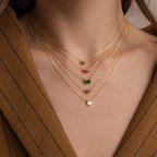 A person wears a brown jacket and layered gold necklaces, including the Custom Cut Birthstone Necklace—a perfect example of personalized jewelry with customizable gemstone pendants.
