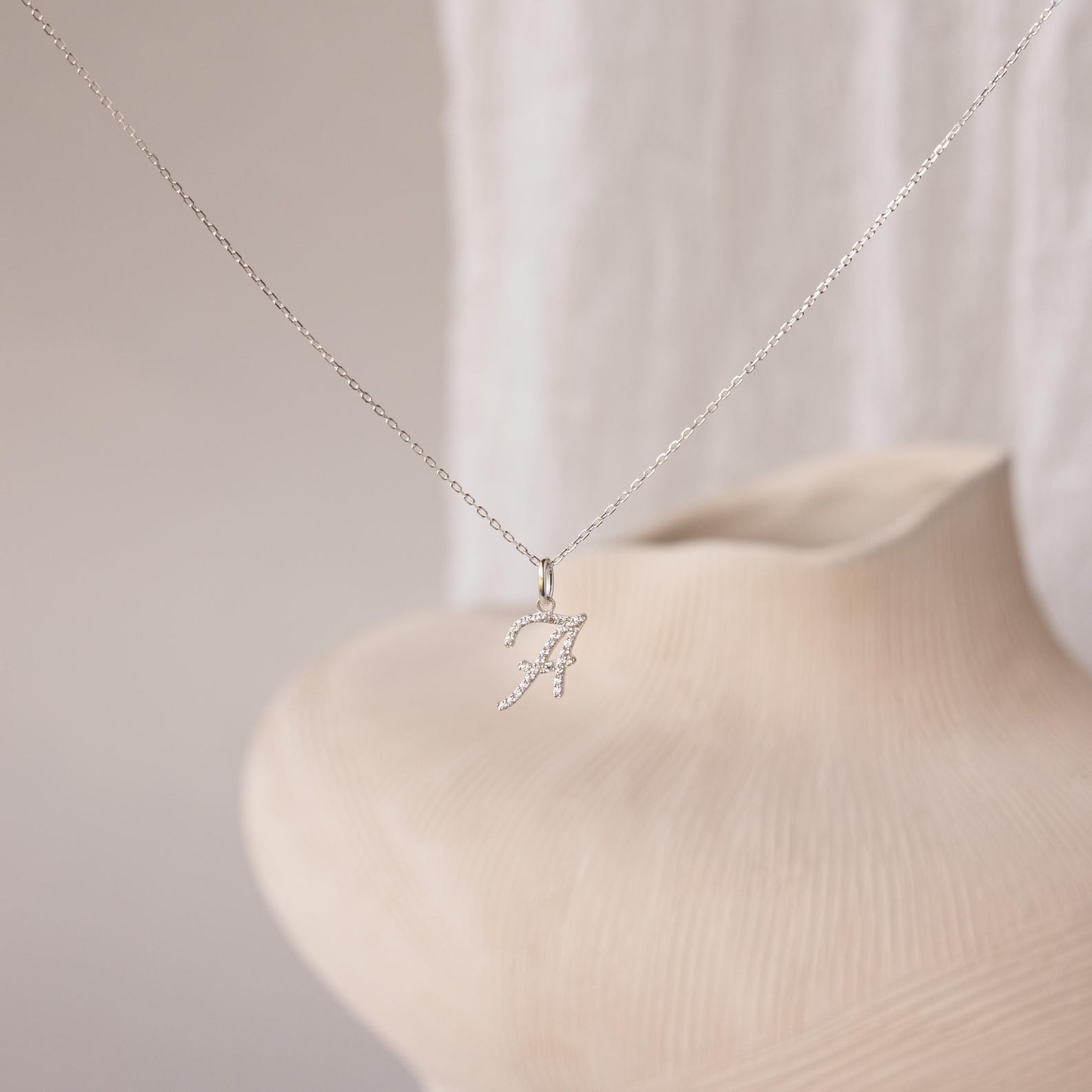 The Large Pave Initial Necklace features a sparkling letter A charm pendant with diamond stones, displayed against a soft, neutral background.