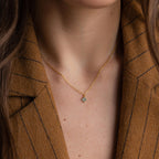 A woman wears the Clover Birthstone Necklace, featuring a small four-leaf clover charm, styled elegantly with a brown pinstripe blazer.