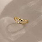 The North Star Curve Dome Ring features diamond star accents and delicate star-shaped engravings, with gemstones shimmering as it casts a soft shadow on a beige surface.