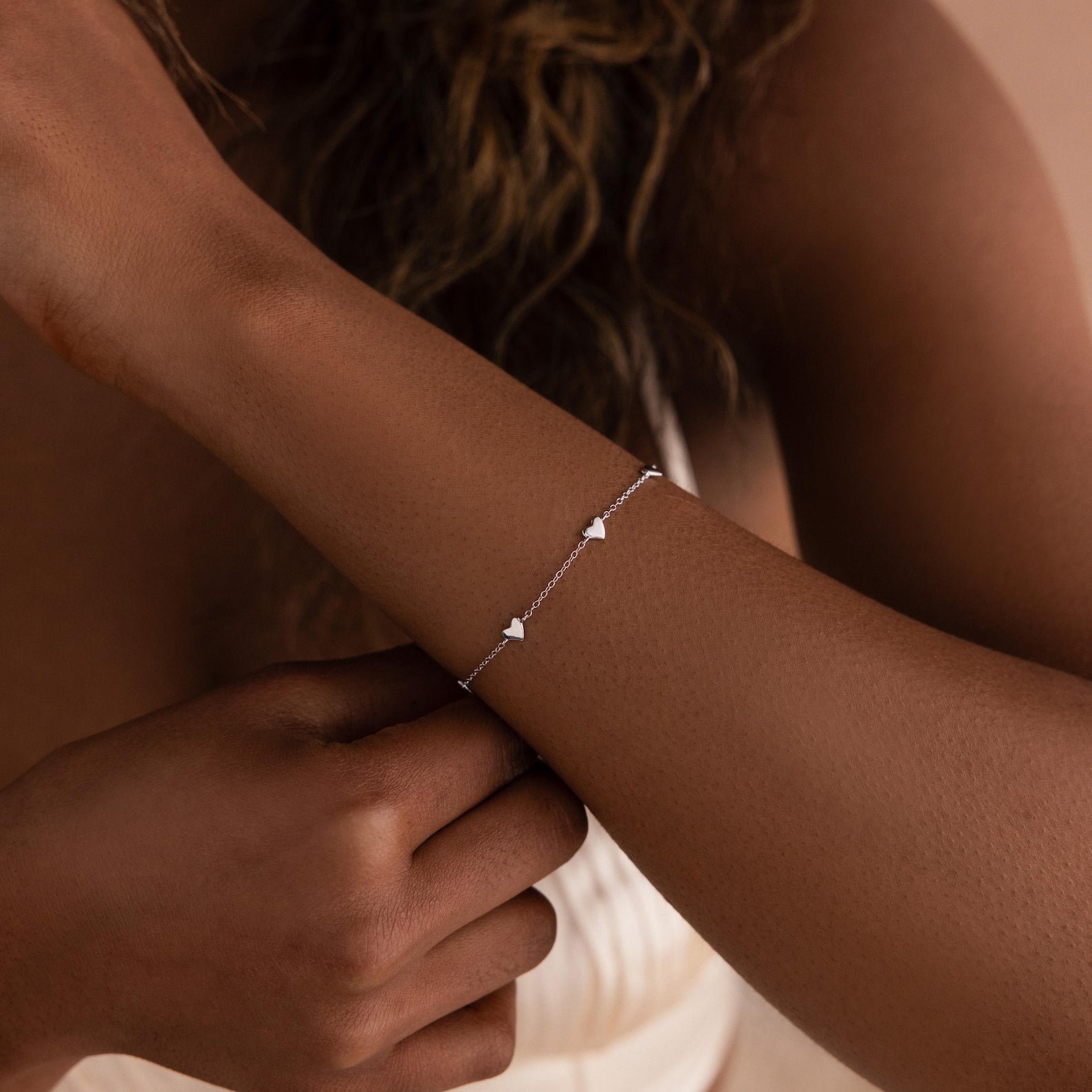 A woman wearing a Heart Station Necklace & Bracelet Set in Sterling Silver adorned with small heart charms on her wrist.