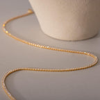 The Dainty Diamond Tennis Necklace & Bracelet Set in 18K Gold, pictured beside a ceramic pot on a beige surface, offers a refined and elegant option for anniversary jewelry.