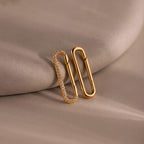The Multipurpose Pave Link Clasp Set in 18K Gold features two paperclip-shaped earrings—one with sparkling stones—displayed on a soft beige surface, offering versatile styling options.