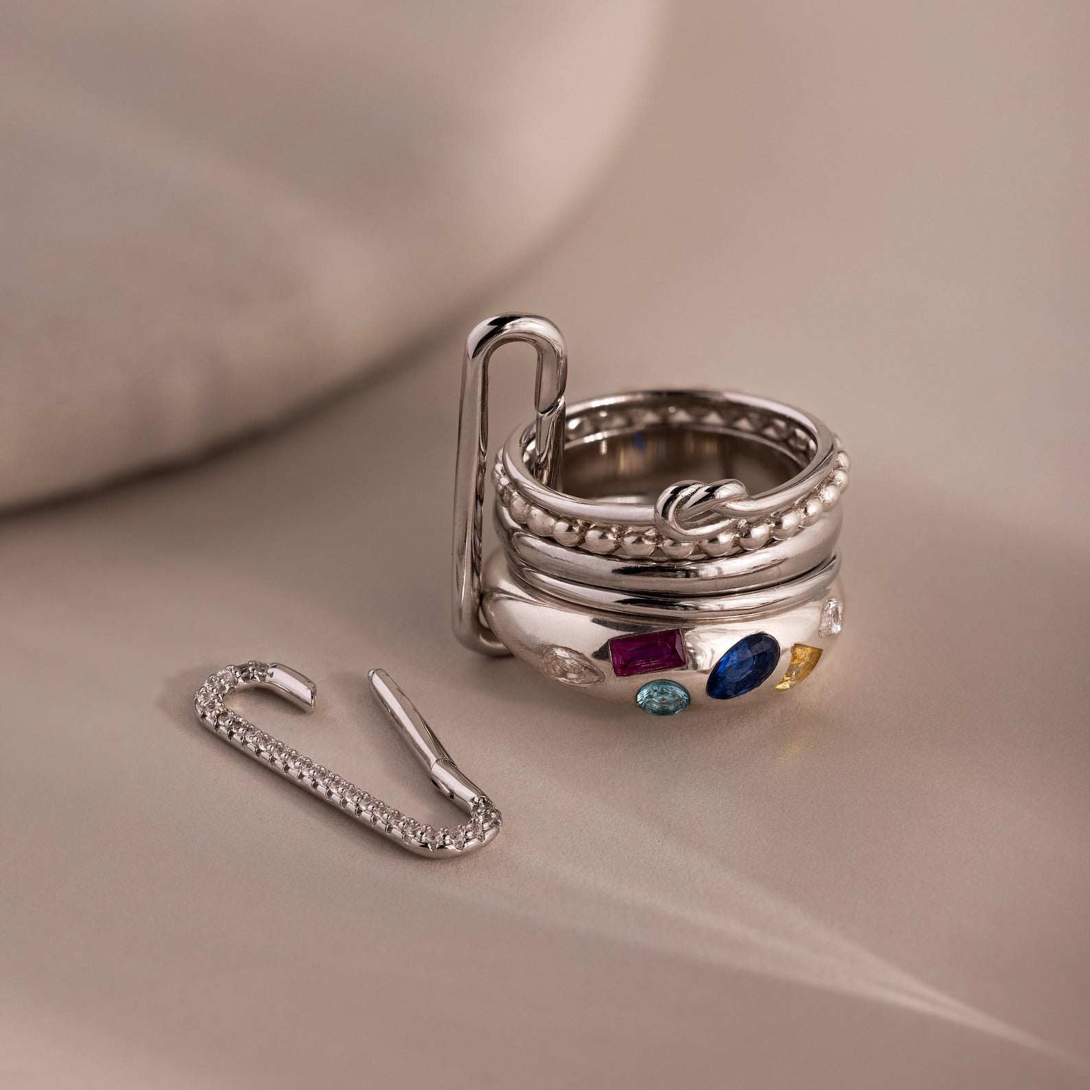 Five silver rings adorned with vibrant gemstones are stacked on a paperclip, next to a jeweled paperclip—perfect for creative jewelry styling or pairing with our Multipurpose Pave Link Clasp Set.