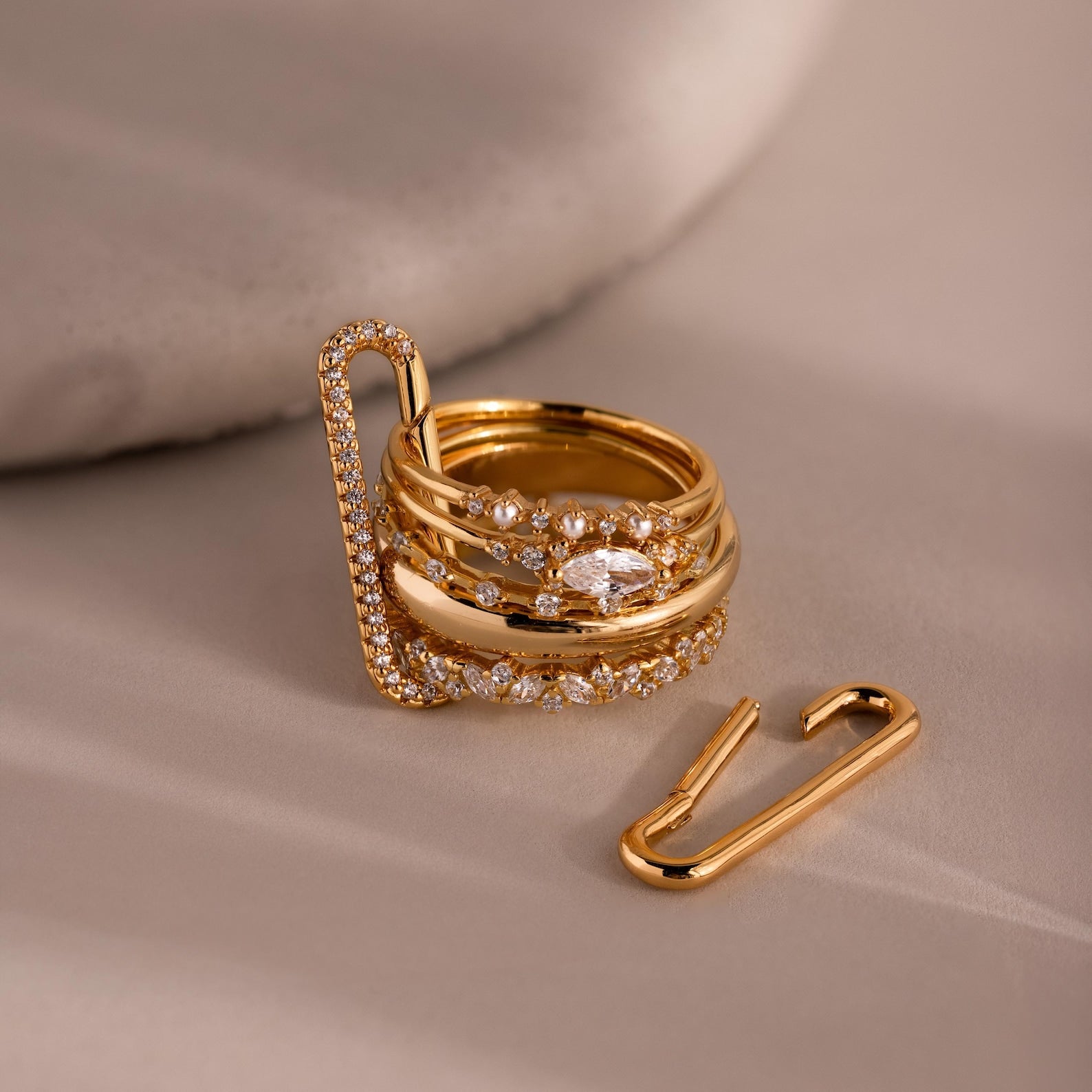 Stacked 18K gold rings with embedded diamonds sit beside the Multipurpose Pave Link Clasp Set in 18K Gold, creating an elegant jewelry styling display on a beige surface.