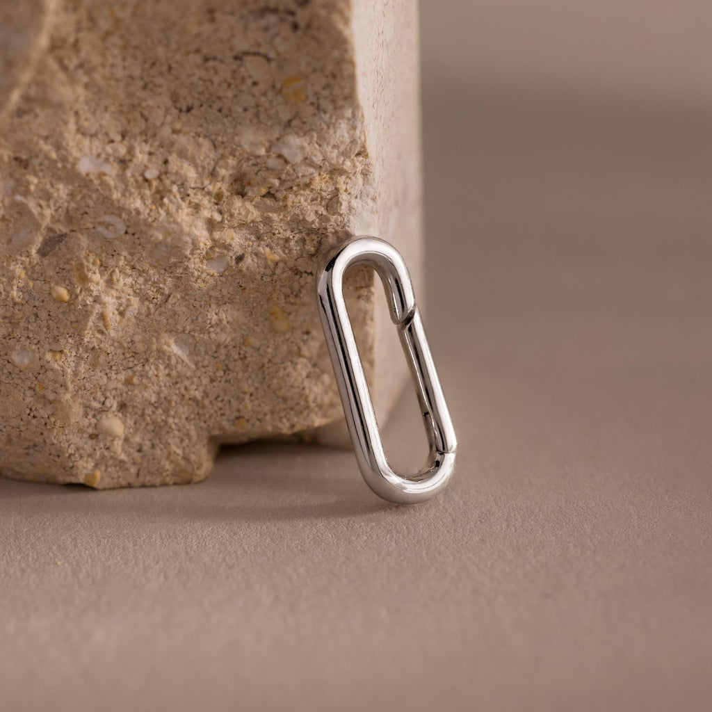 A silver oval-shaped link from the Multipurpose Mixed Metal Clasp Set is displayed on a textured beige stone atop a smooth surface.