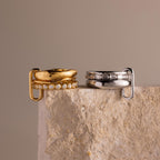 The Multipurpose Mixed Metal Clasp Set features two stacked rings—one 18k gold, one silver—each adorned with diamonds, displayed elegantly on a textured stone surface. Ideal for effortless ring stacking.